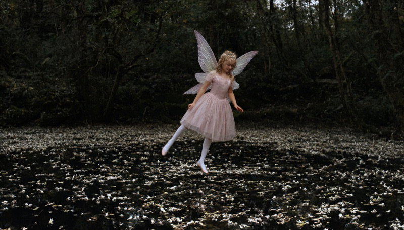 A fairy in a pink dress stands in a dark forest pond